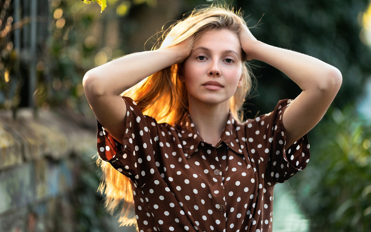 Девушка в рубашке в горох с руками в волосах 