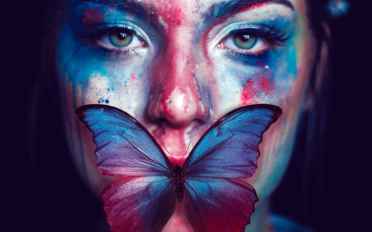 Лицо девушки в краске с бабочкой во рту