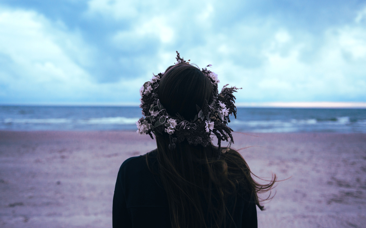 Девушка с венком на голове на фоне моря вид сзади