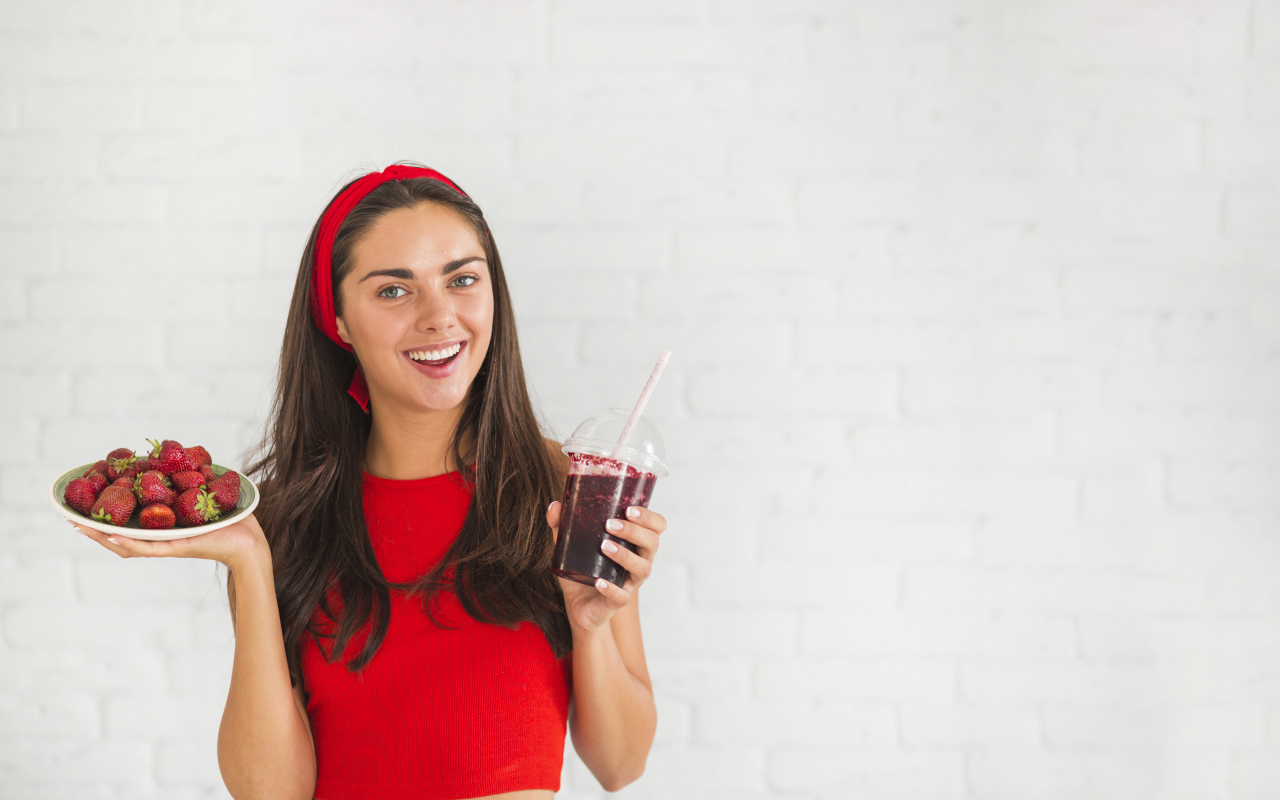 Улыбающаяся девушка с клубникой и смузи в руках