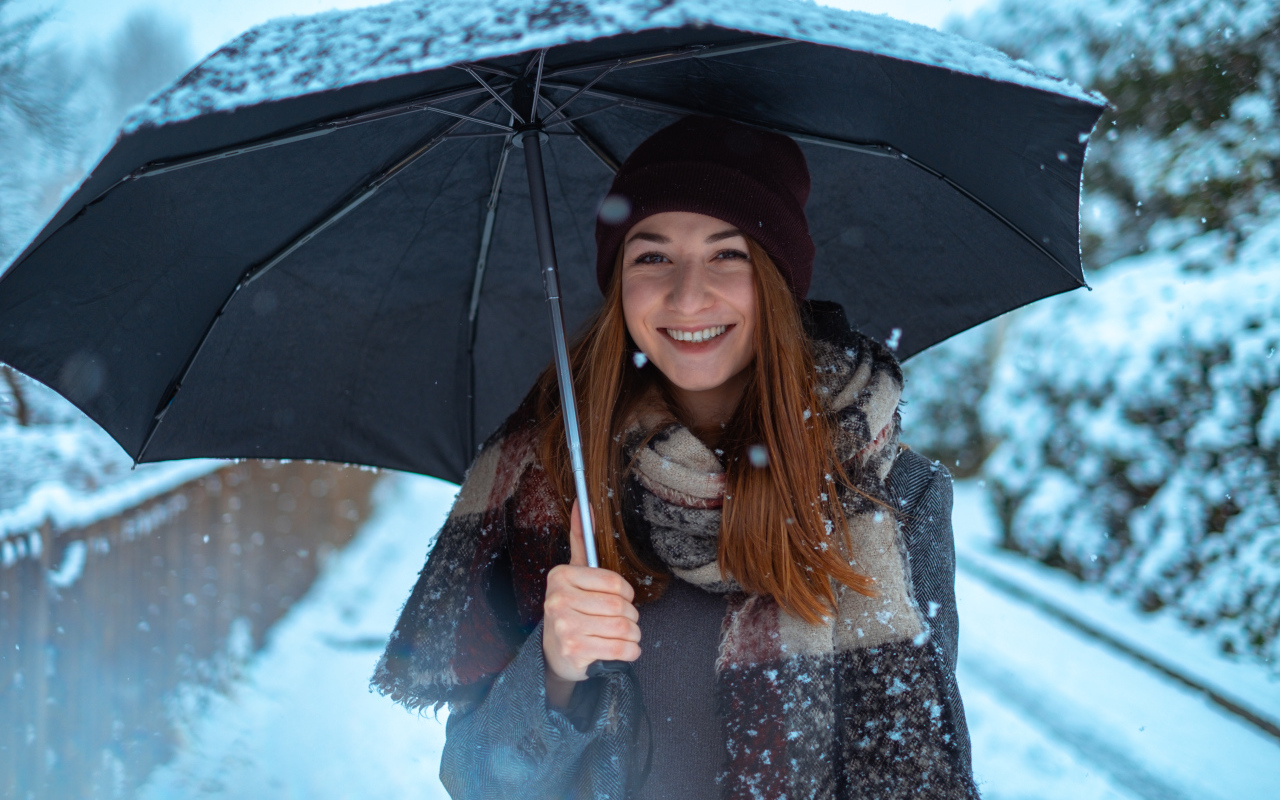 Улыбающаяся молодая девушка под зонтом зимой