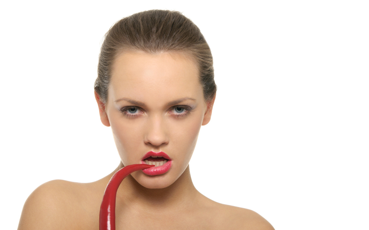 Молодая девушка кусает красный перец на белом фоне