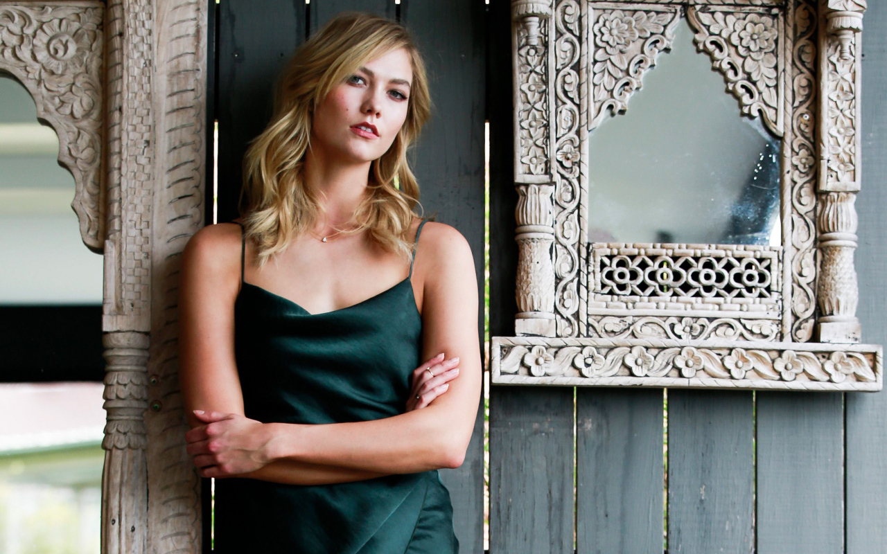 Красивая стильная модель Карли Клосс стоит у стены с зеркалом