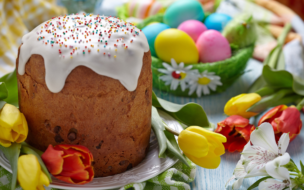 Пасхальный кулич на столе с тюльпанами и крашеными яйцами