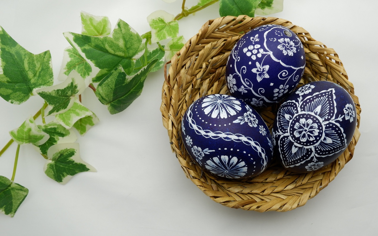 Three painted eggs in a basket on a table with a branch