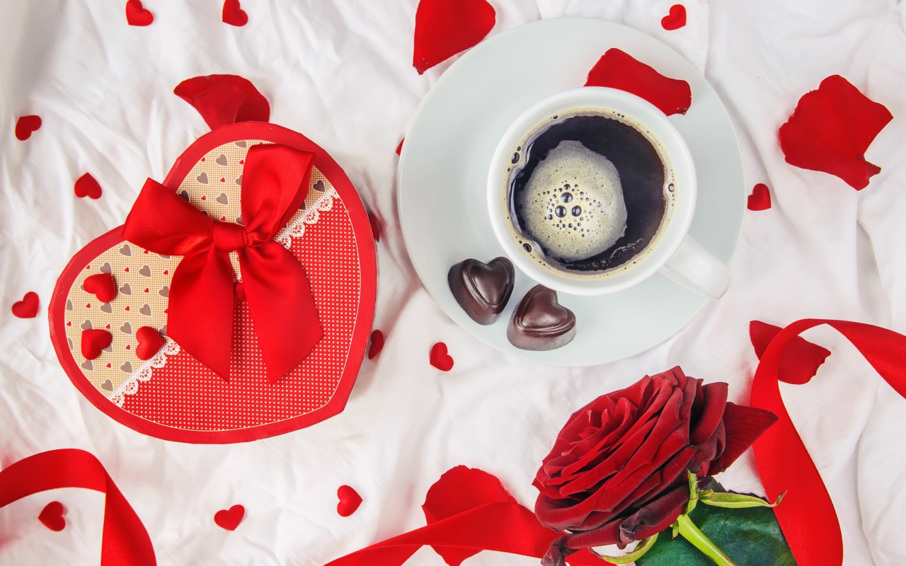 Кружка с кофе и шоколадными конфетами на столе с подарком и красной розой 