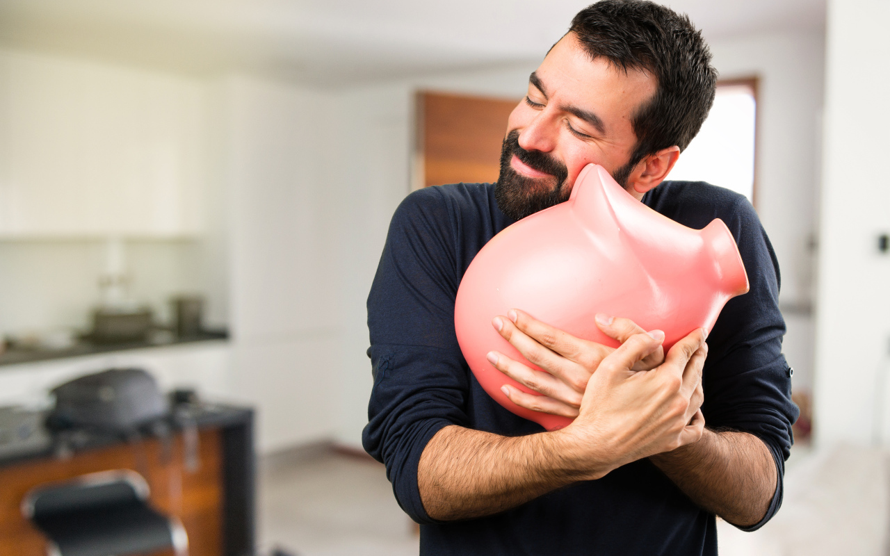 Мужчина обнимает розовую свинью копилку 