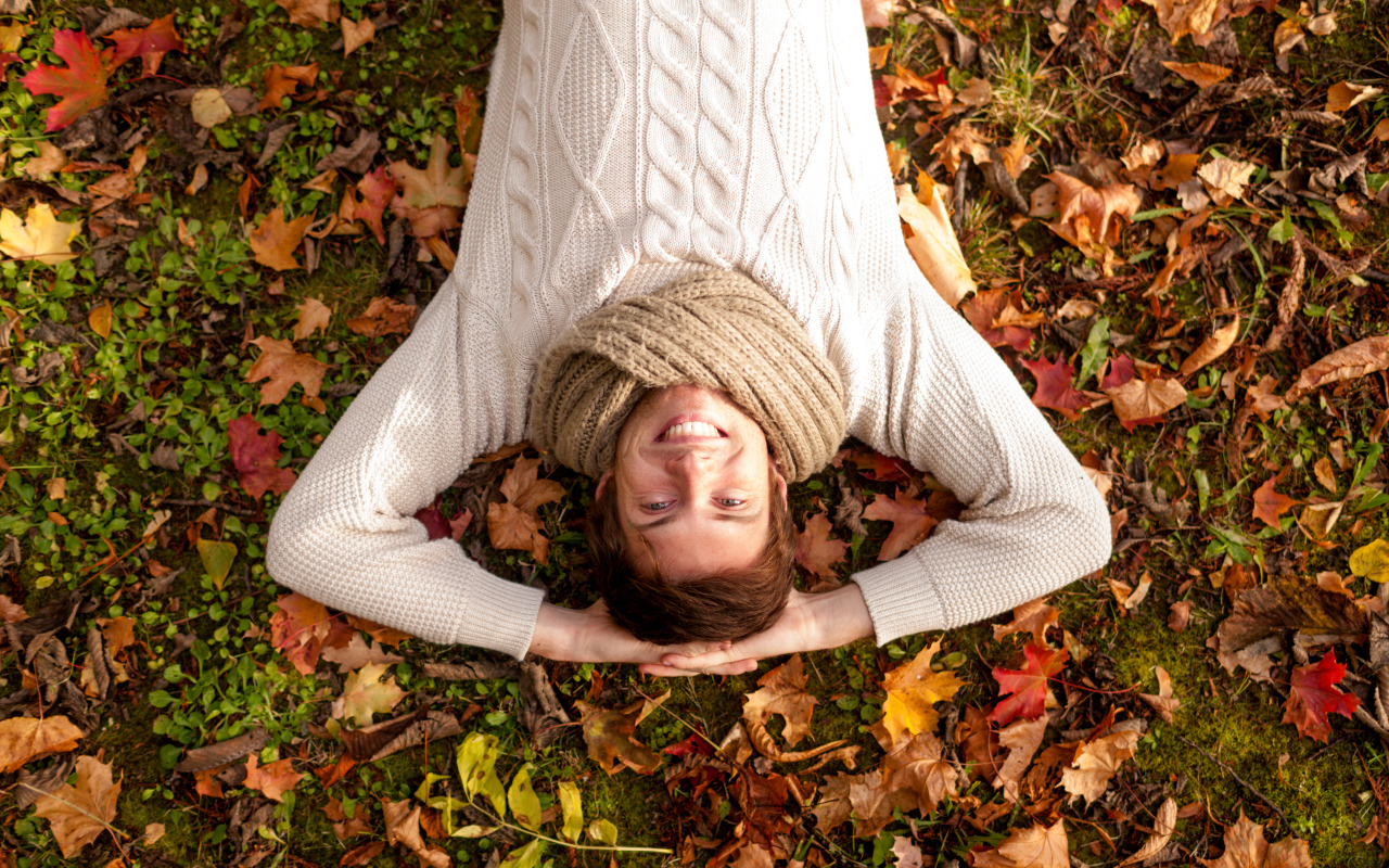 Улыбающийся мужчина в свитере лежит на опавших листьях 