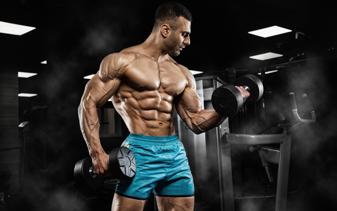 Сильный накаченный мужчина в шортах с гантелями в руках 