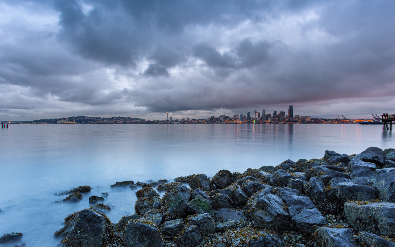 Камни на берегу реки на фоне города под пасмурным небом