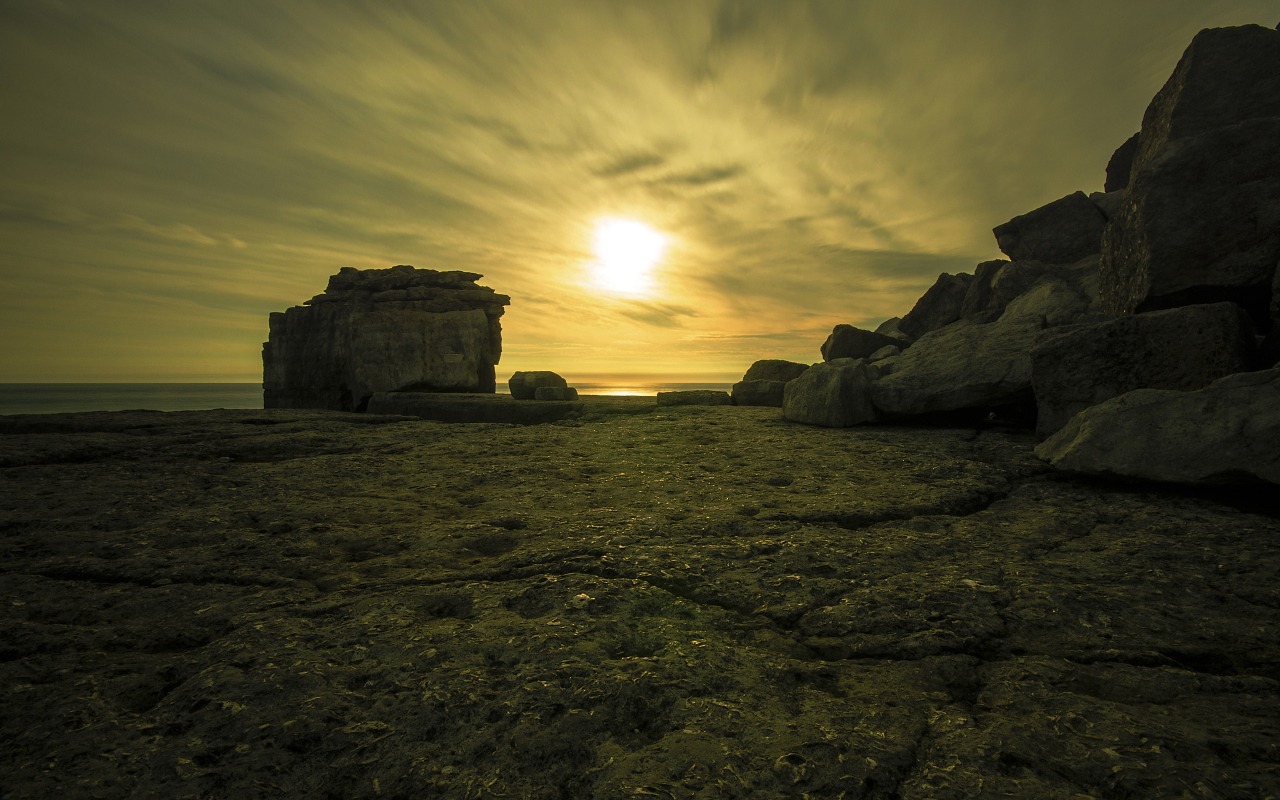 Солнце в облаках освещает камни у моря