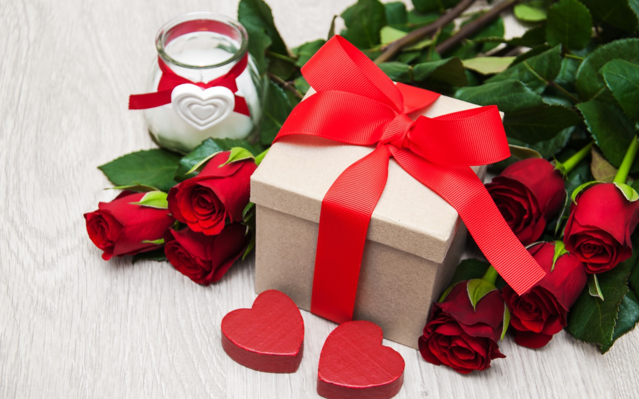 Красивый букет красных роз на столе со свечой и подарком