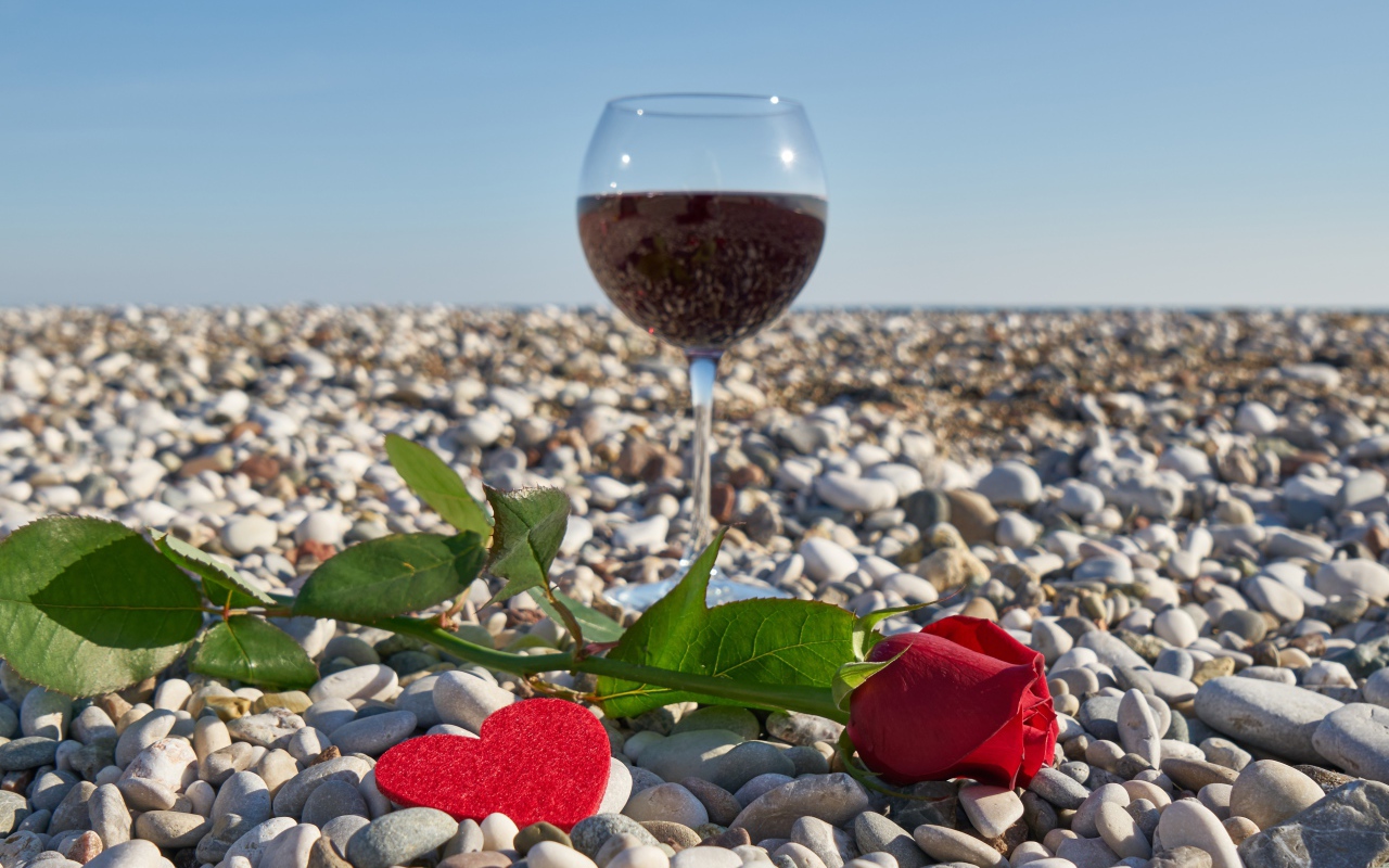 Красная роза на морской гальке с сердечком и бокалом вина