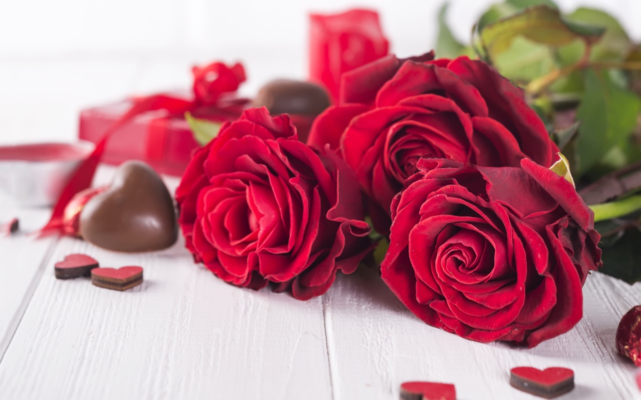 Три красивые красные розы на столе с конфетами