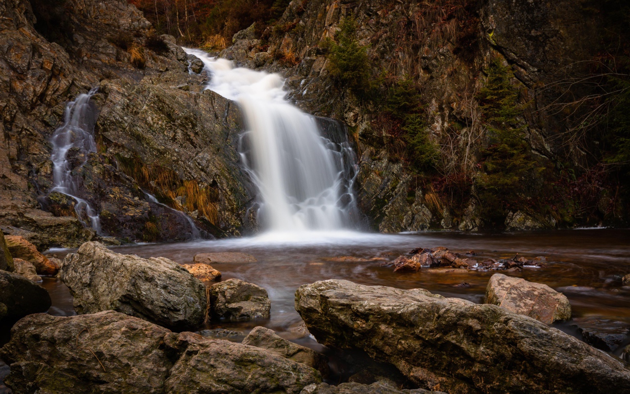 Быстрая вода водопада стекает по камням в горную реку