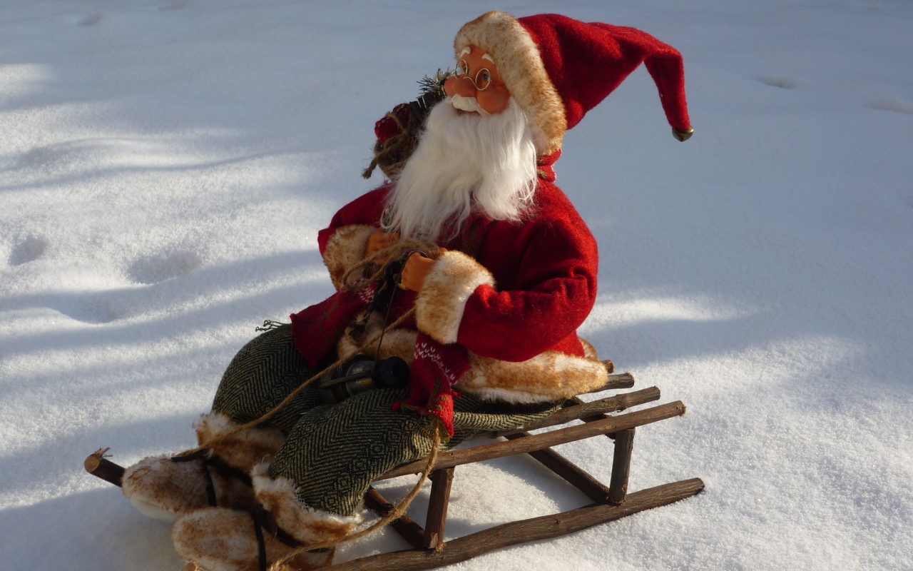 Игрушка деда Мороза на санках стоит на снегу