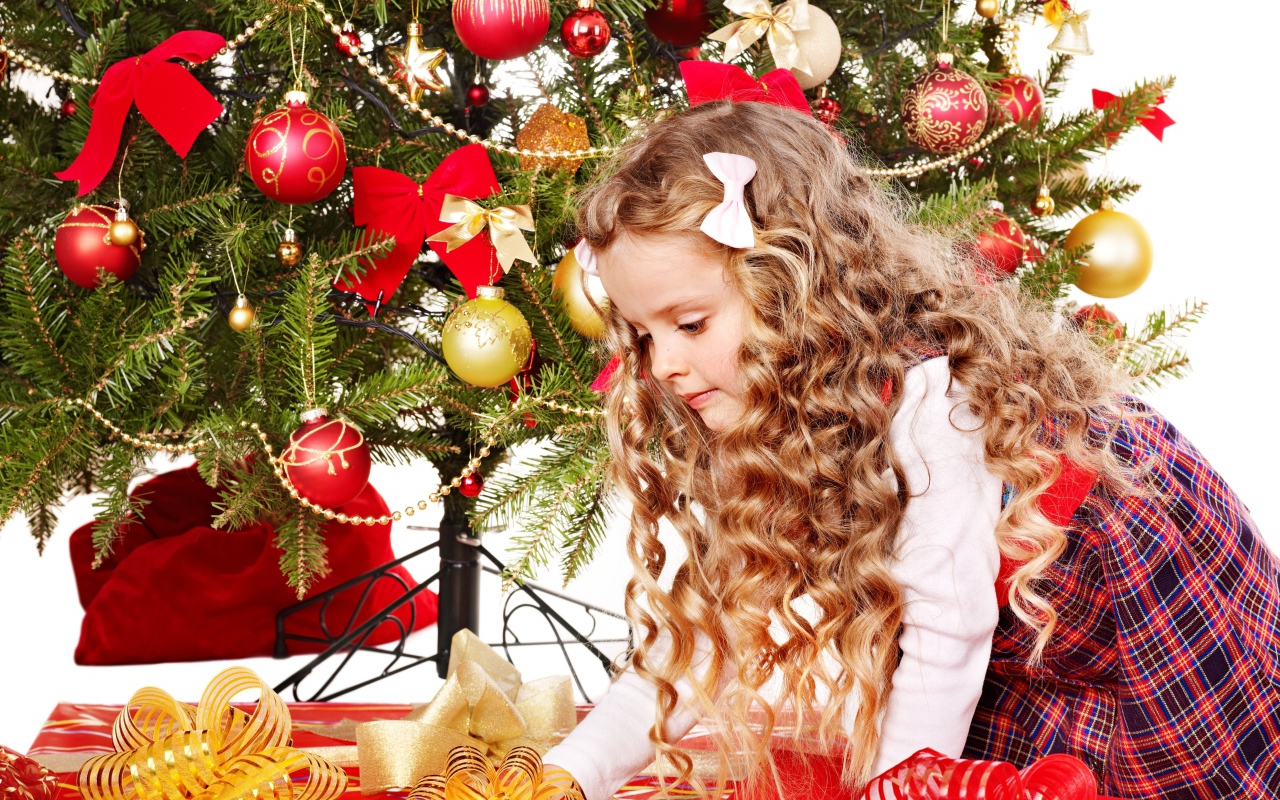 Красивая маленькая девочка смотрит подарки под елкой на новый год 