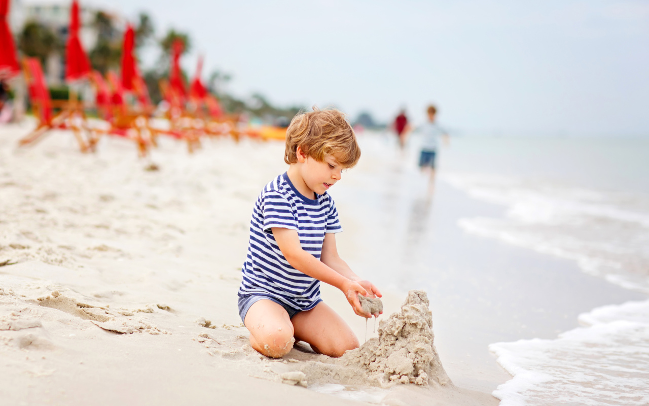 Маленький мальчик строит замок из песка на пляже