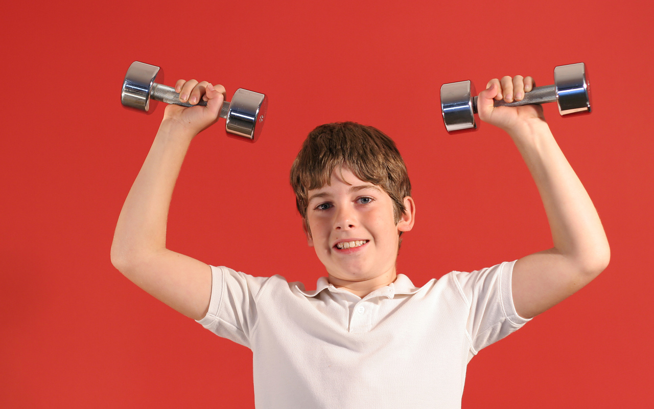 Маленький мальчик с гантелями на красном фоне