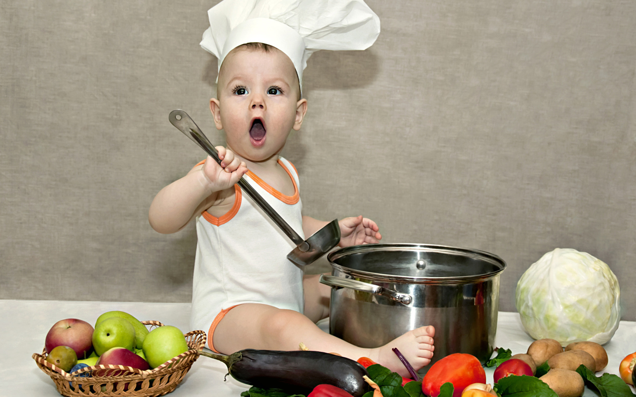 Маленький поваренок с кастрюлей на столе с овощами