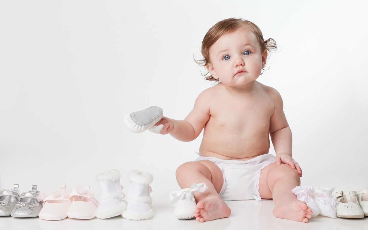 Маленький забавный голубоглазый малыш с обувью на белом фоне