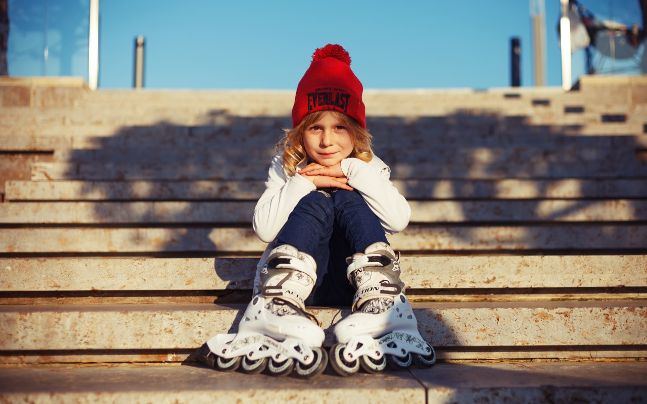 Маленькая девочка в роликах сидит на ступеньках 