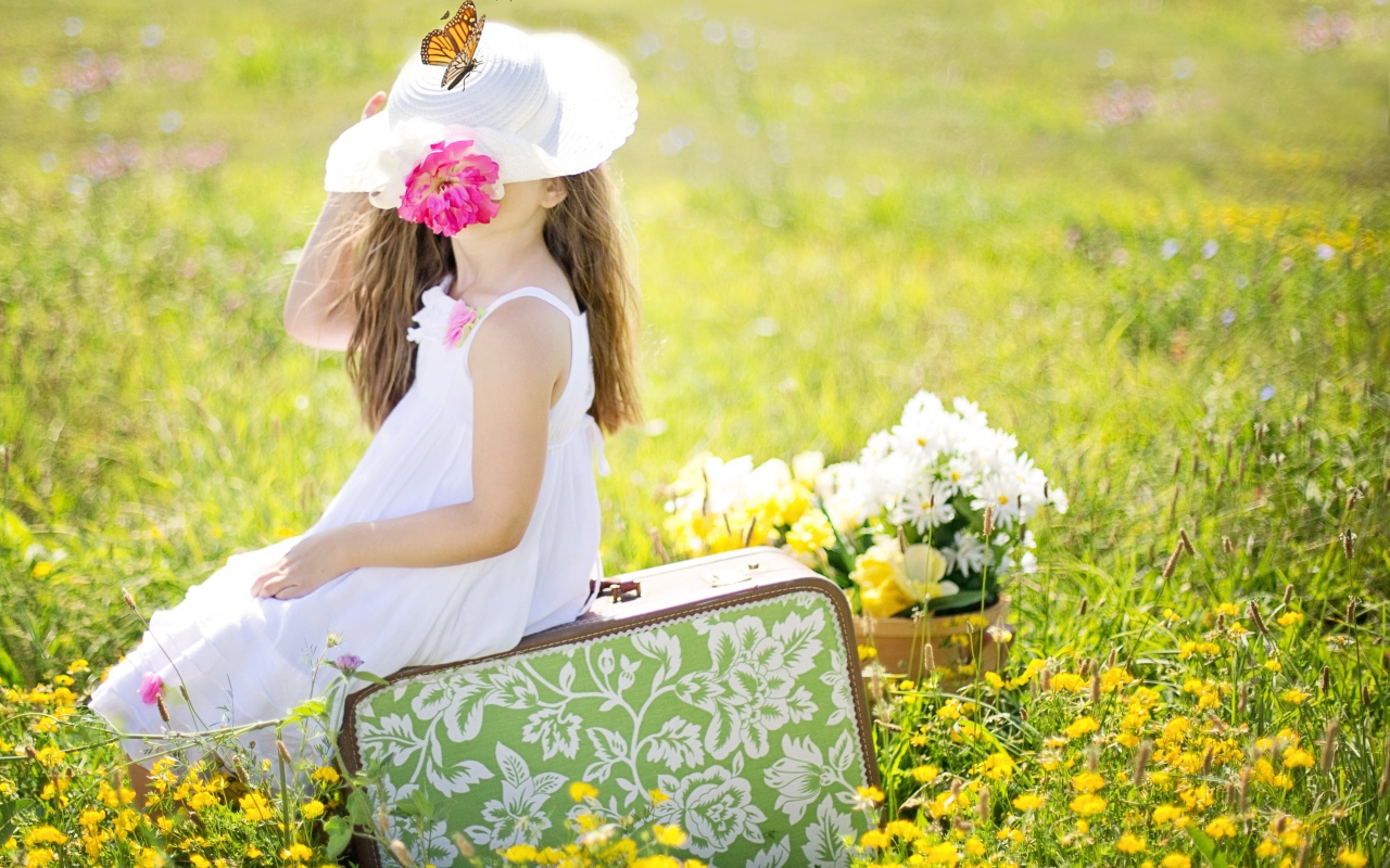 Маленькая девочка сидит на чемодане на поле с цветами