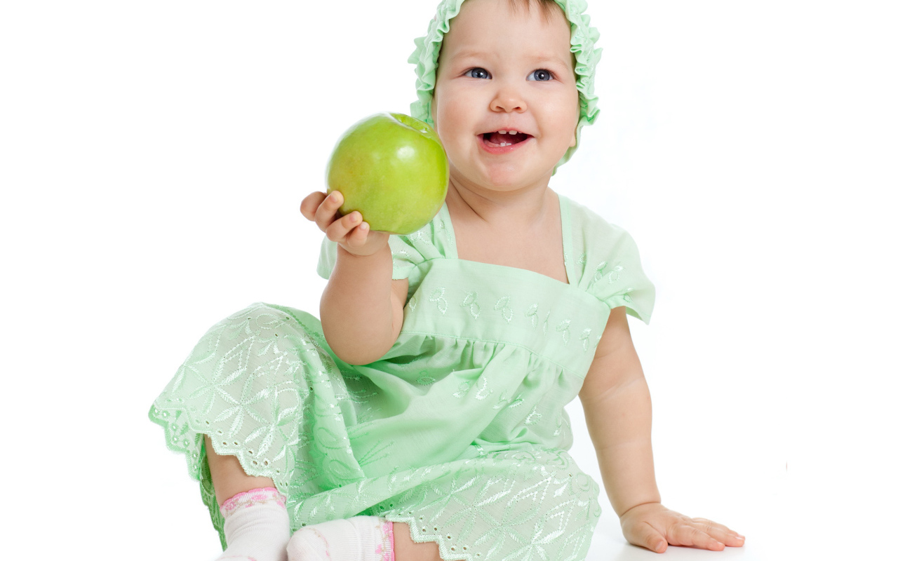 Улыбающаяся маленькая девочка в красивом платье с зеленым яблоком в руке