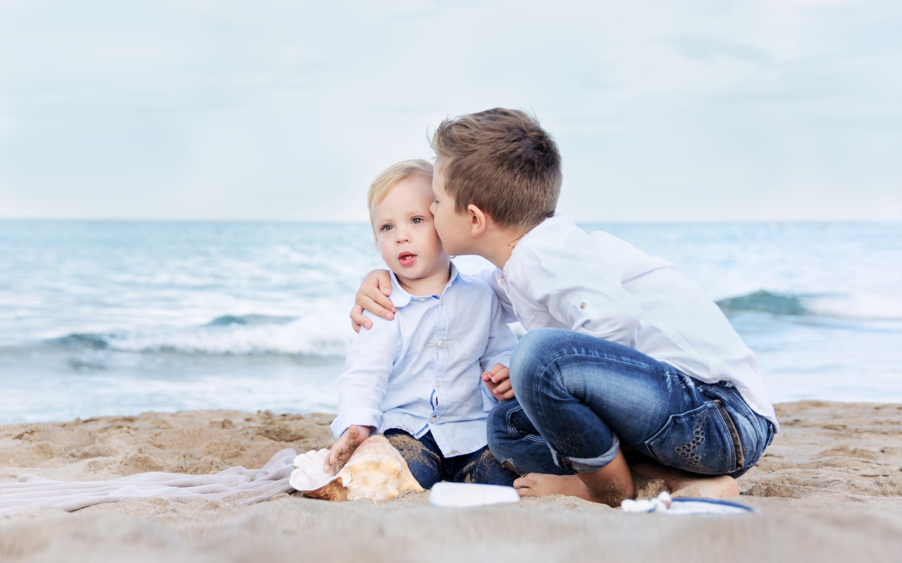 Два маленьких брата сидят на песке на пляже
