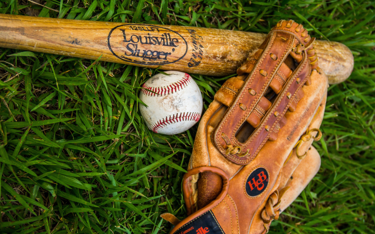 Бейсбольная бита, перчатка и мяч лежат на зеленой траве
