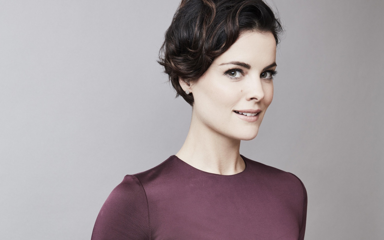 Улыбающаяся девушка, актриса Джейми Александр на сером фоне