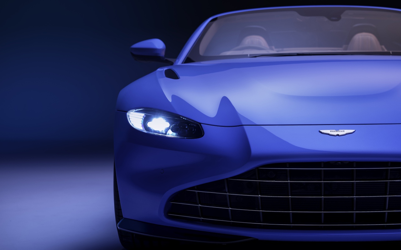 Синий автомобиль Aston Martin Vantage Roadster 2020 года с включенной фарой 