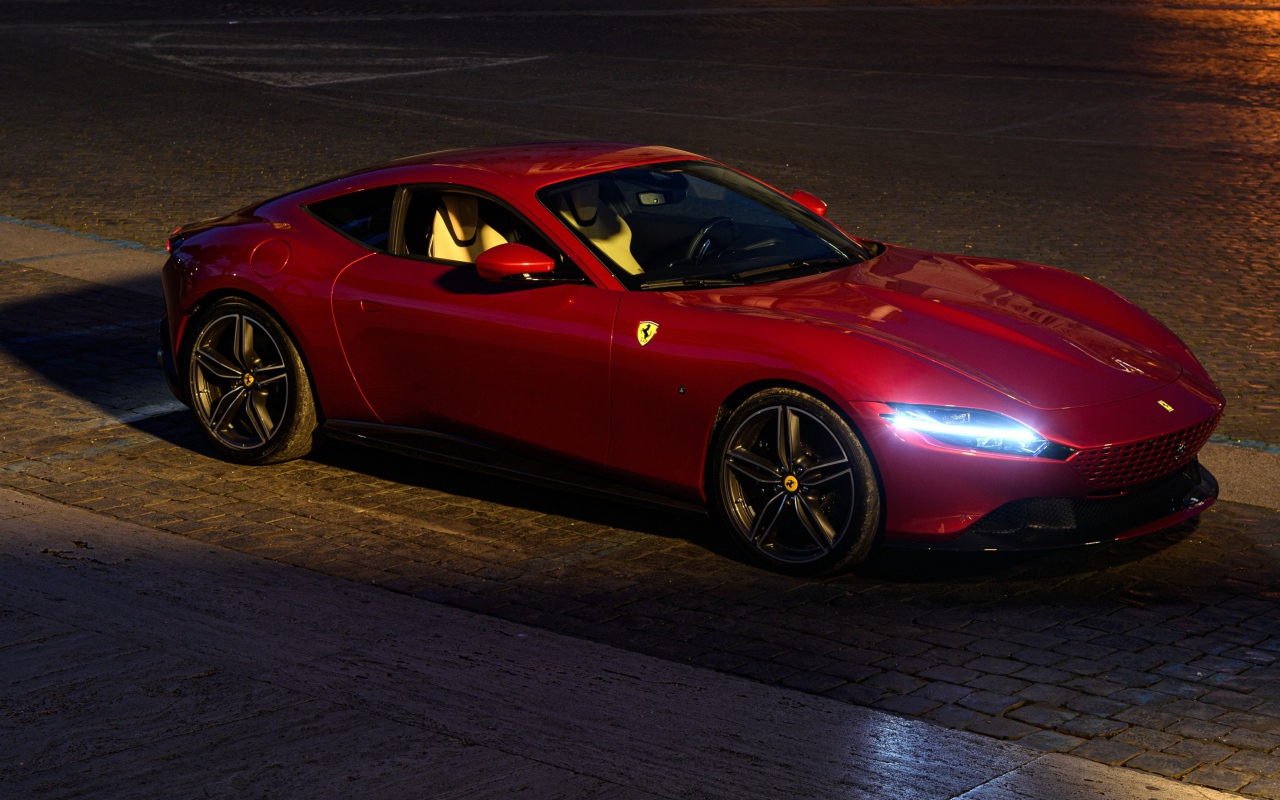 Красный автомобиль Ferrari Roma 2020 года с включенными фарами вечером