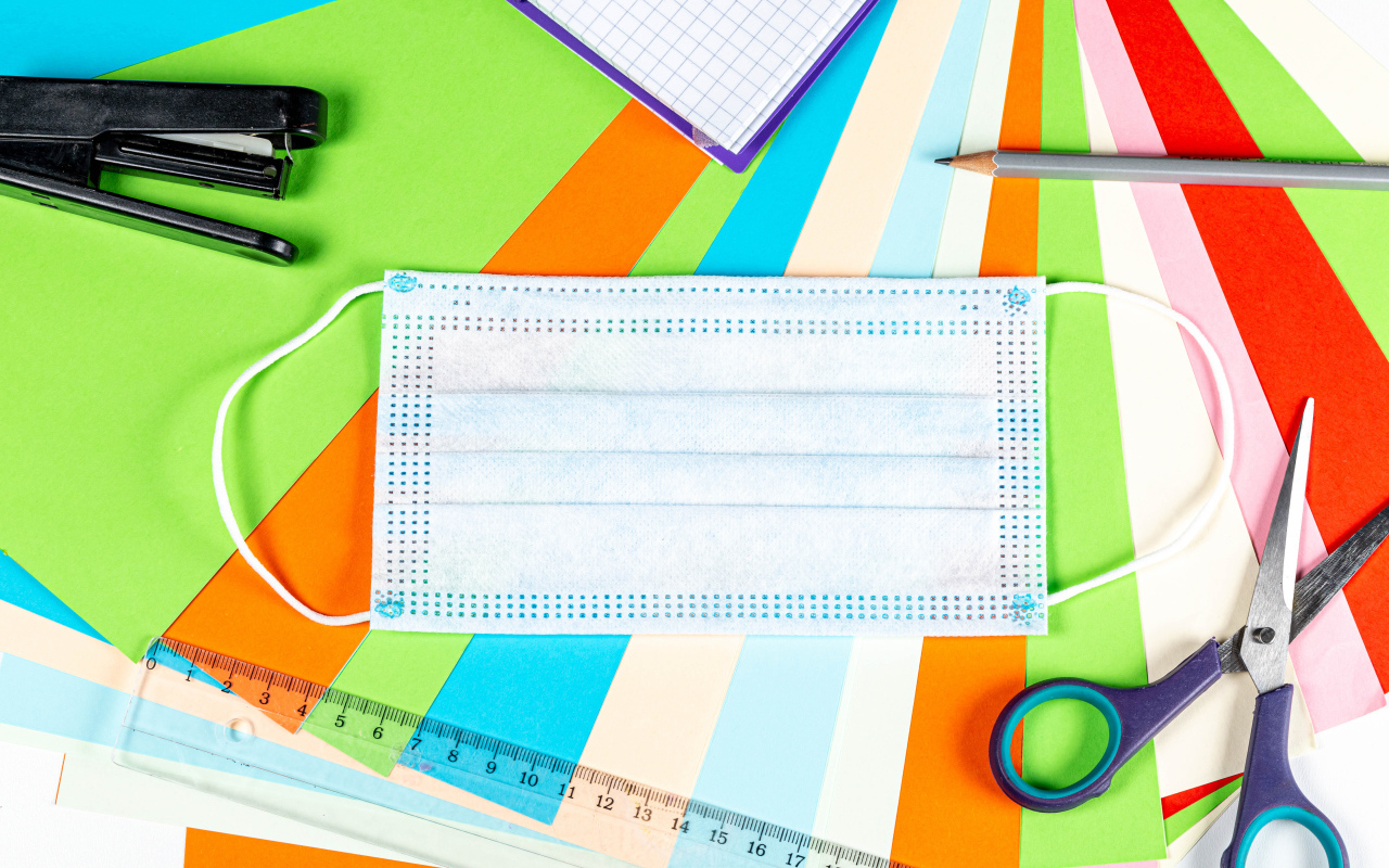 Маска от коронавируса лежит на цветной бумаге с канцелярскими предметами