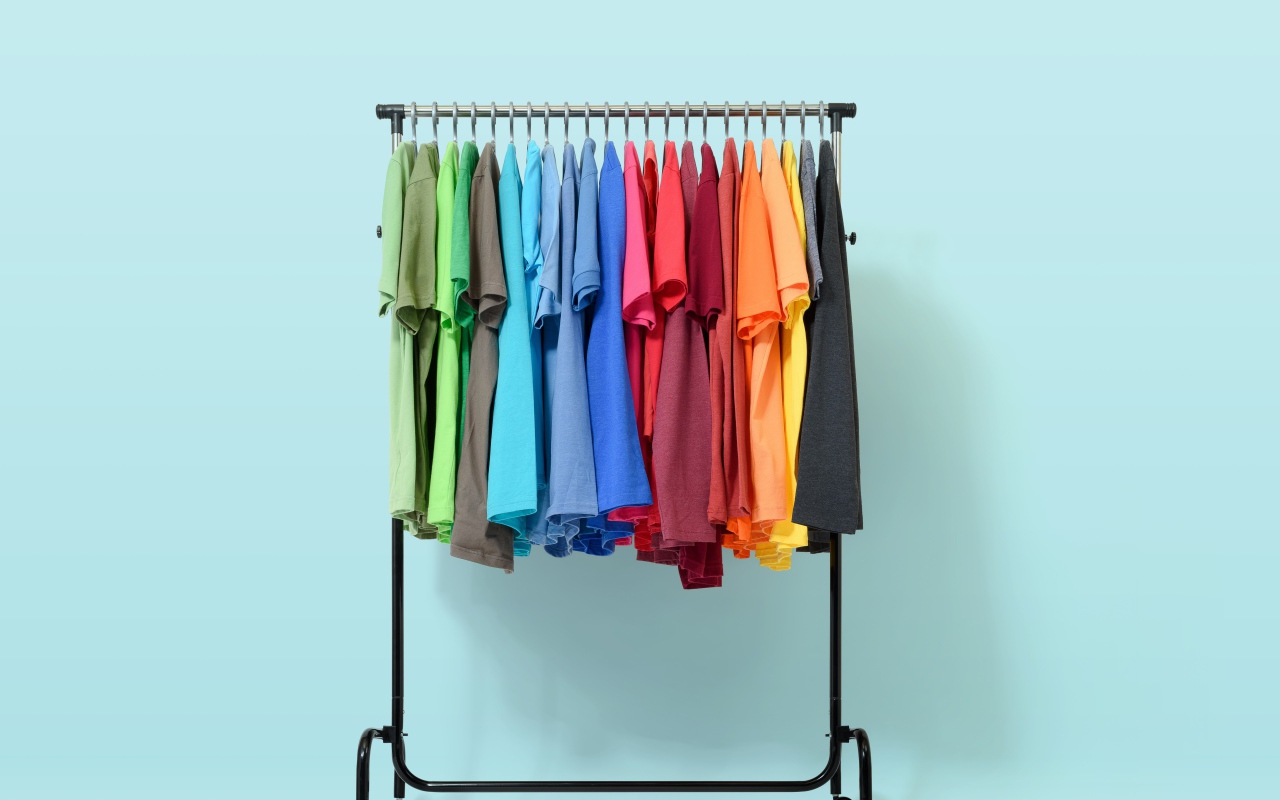 Разноцветные футболки на вешалке на голубом фоне