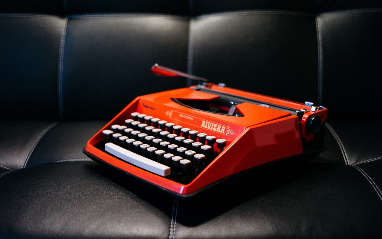 Старая красная печатная машинка на черном диване