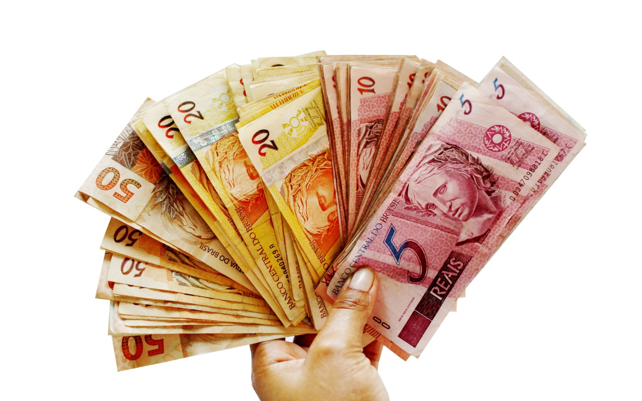 Много купюр бразильского реала в руке на белом фоне 