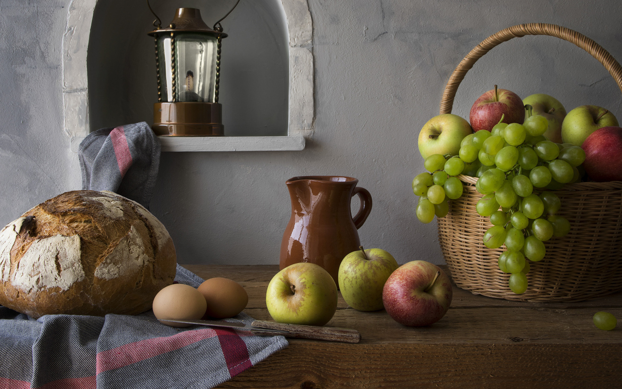 Basket with apples and grapes on a table with bread and eggs