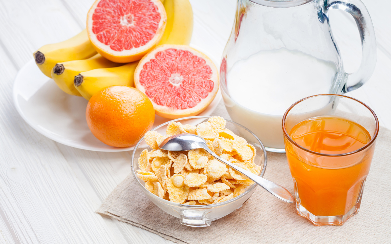 Кукурузные хлопья на столе с молоком, соком и свежими фруктами на завтрак