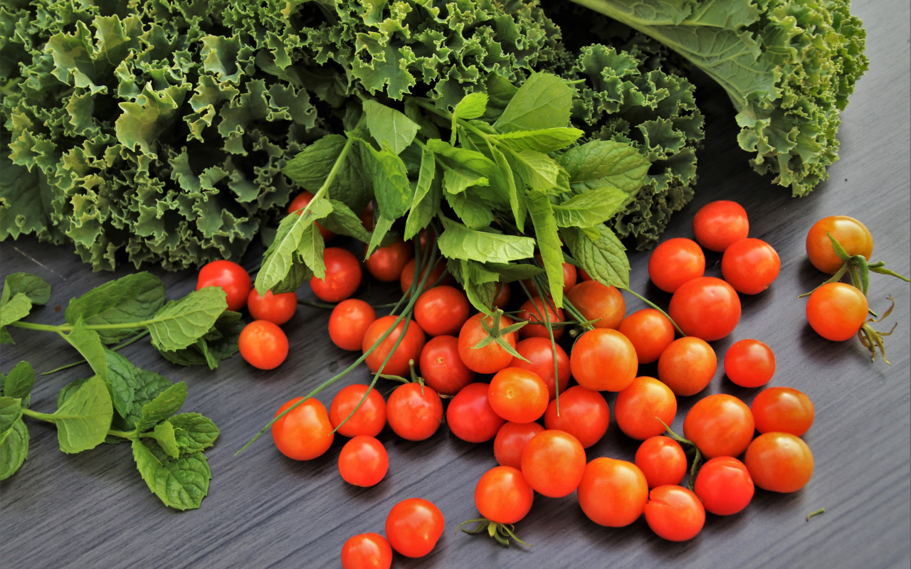Красные мелкие помидоры на столе с зеленью 