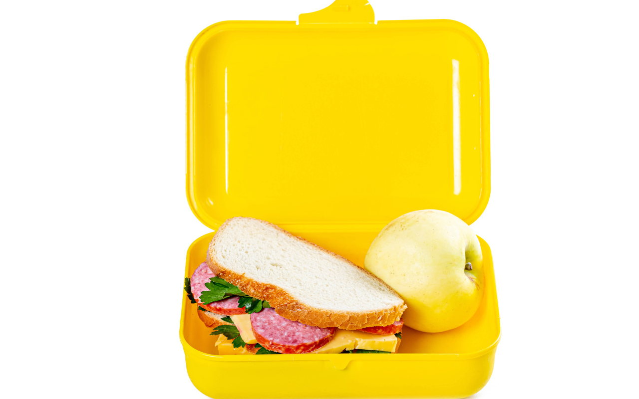 Бутерброд и яблоко в контейнере на белом фоне