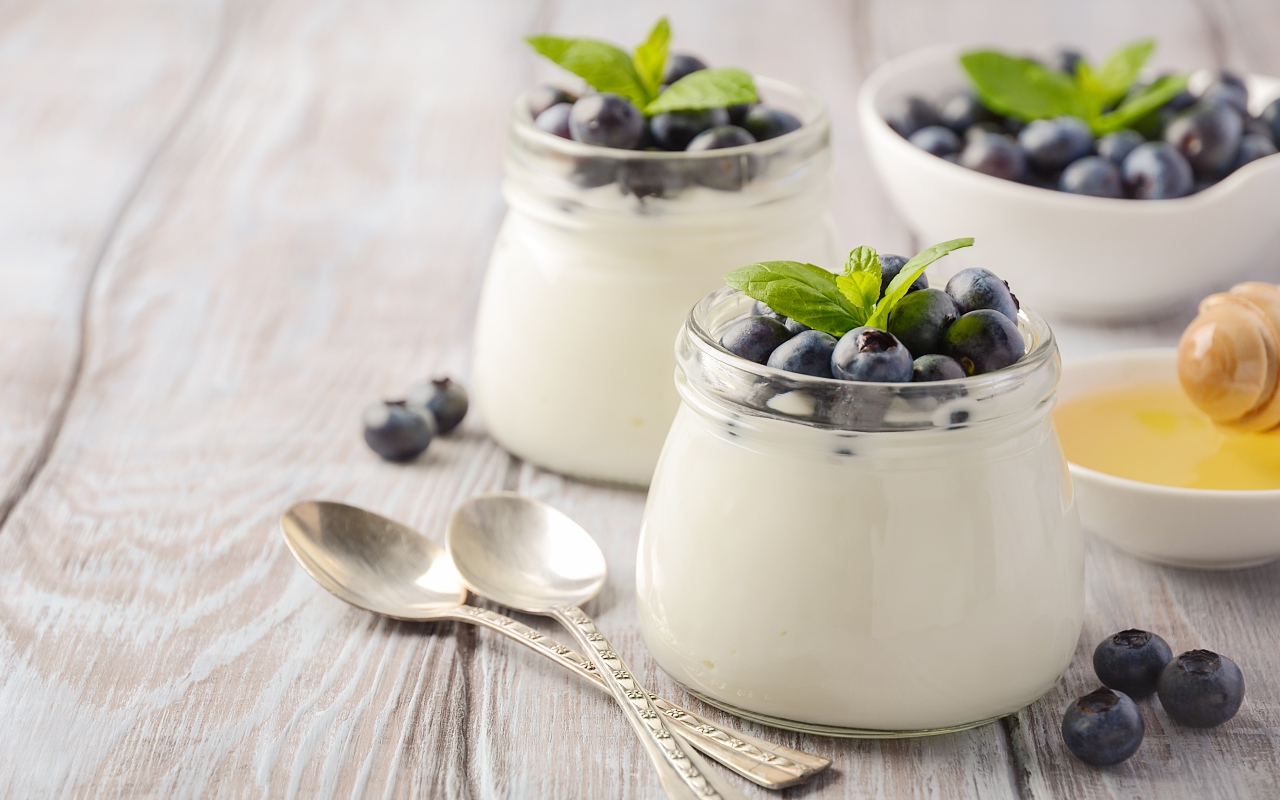 Йогурт в банках с ягодами черники на столе с ложками и медом