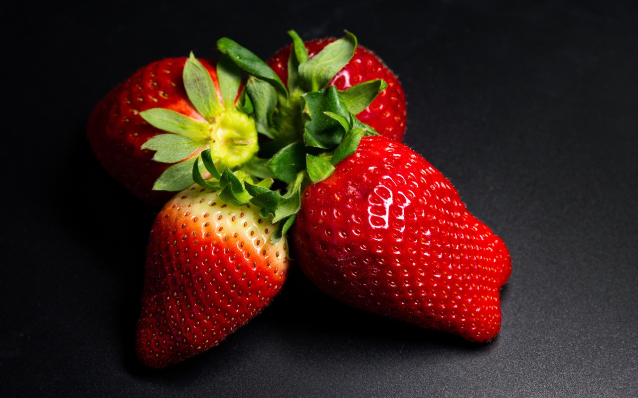 Четыре спелых красных ягоды клубники на черном столе 