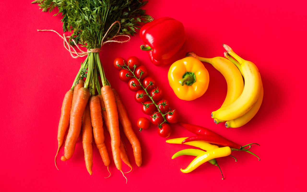 Свежие морковь, помидоры, перец и бананы на красном фоне