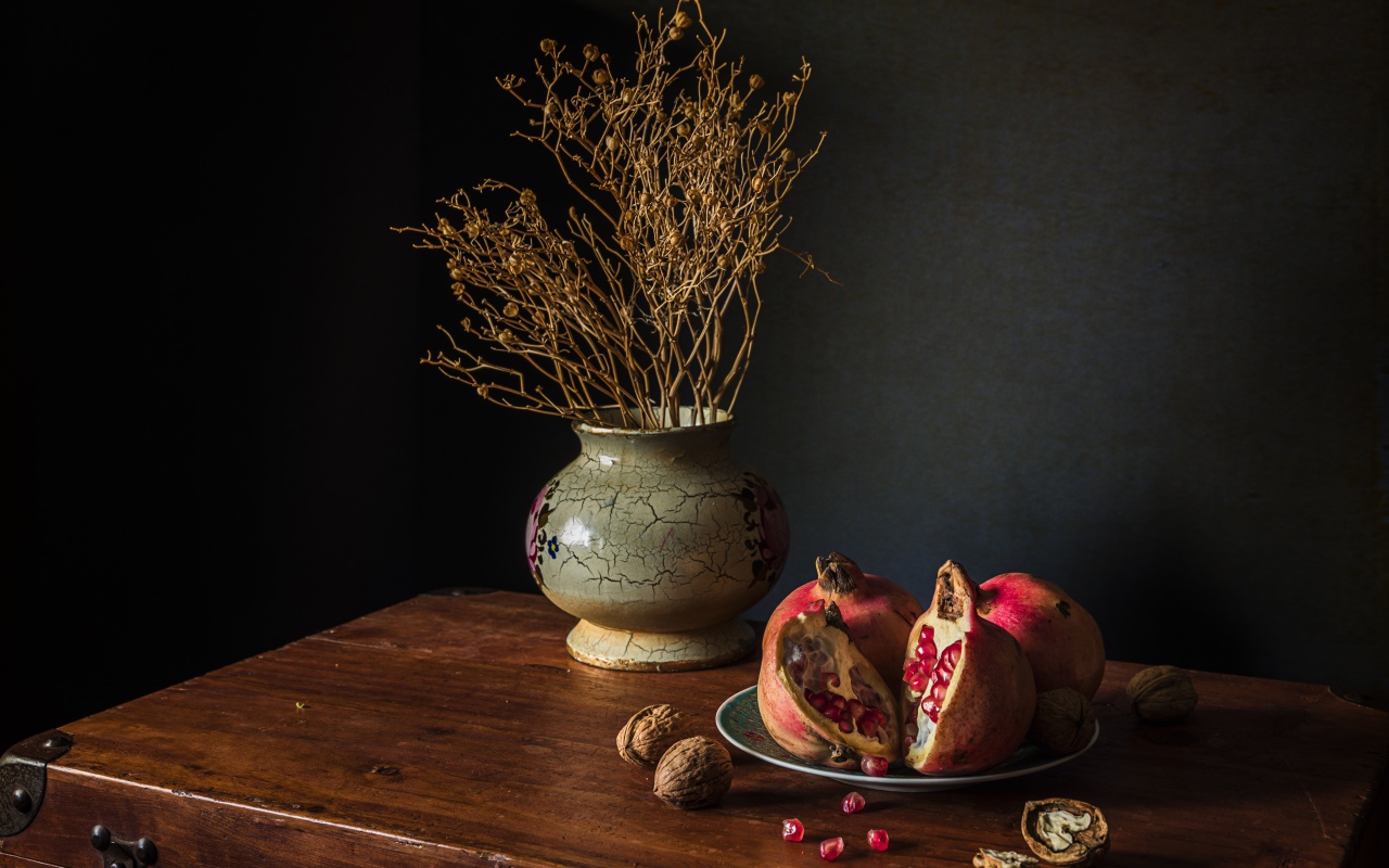 Красный гранат на столе с грецкими орехами и сухой веткой в вазе