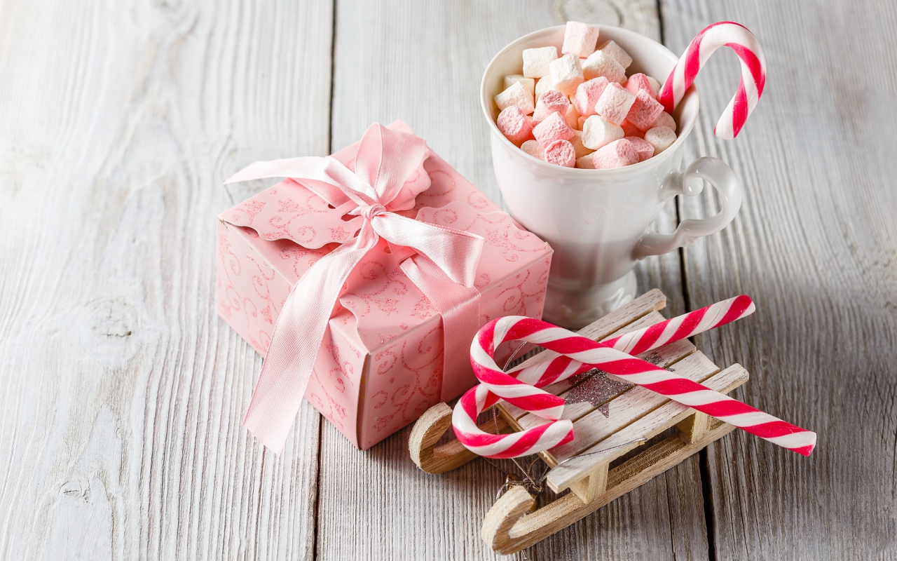 Чашка с маршмеллоу на столе с игрушечными санками и подарком