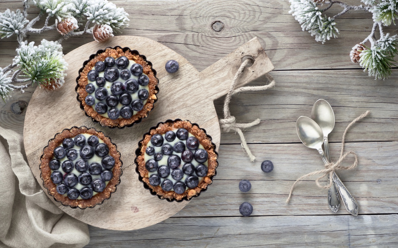 Кексы с кремом и ягодами черники на столе с чайными ложками