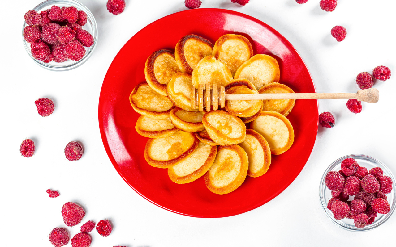 Оладьи на красной с медом на красной тарелке на столе с ягодами малины