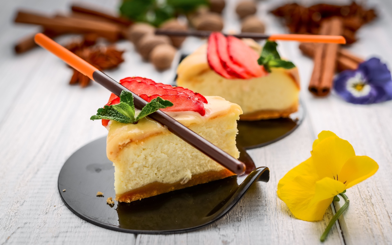 Два куска чизкейка с клубникой на столе с палочками