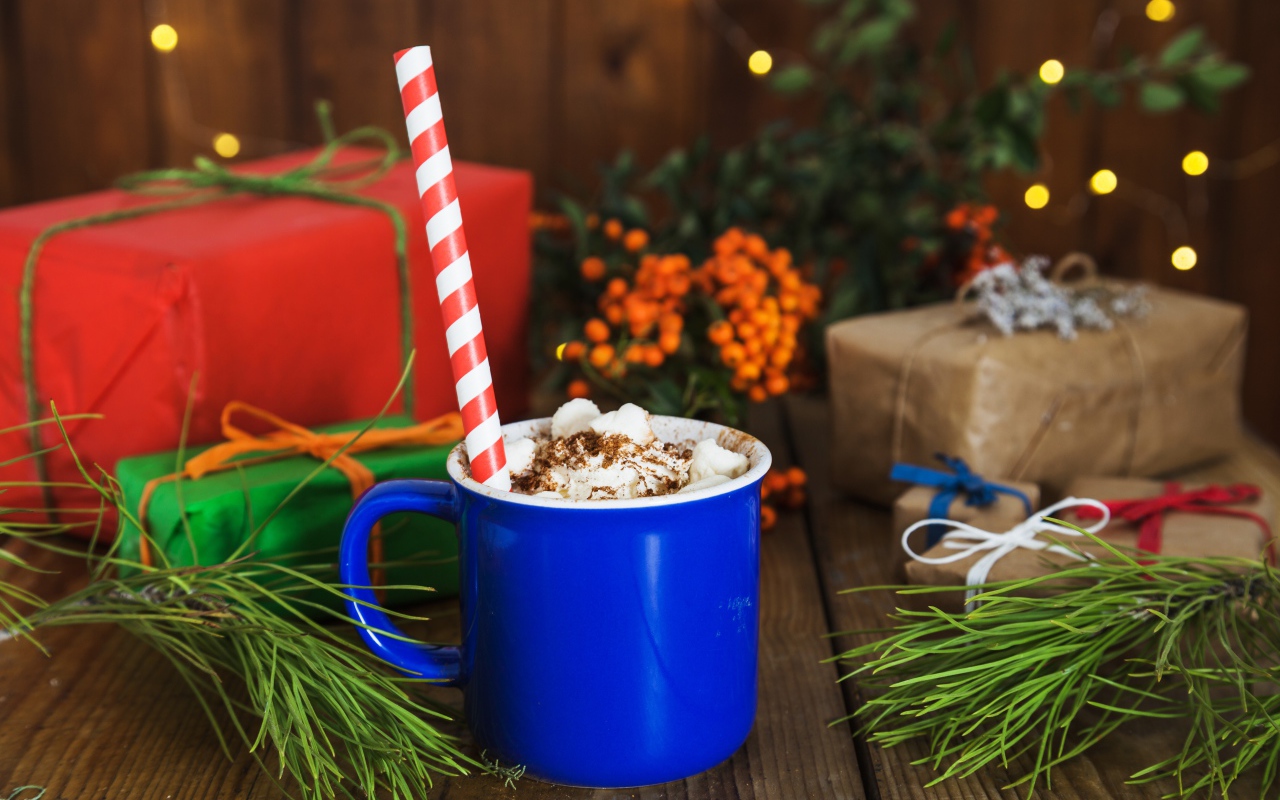 Синяя чашка горячего шоколада с маршмеллоу на столе с еловыми ветками и подарками